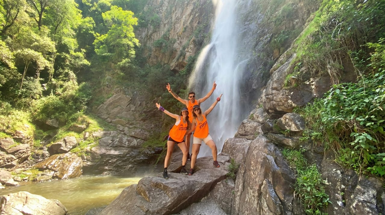 La caída de agua entre el paredón de roca y la vegetación, con gente sobre las piedras