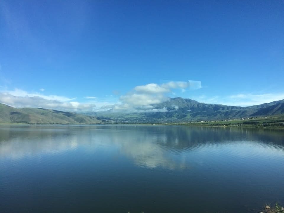 El dique La Angostura espejado, con los cerros del valle y nubes bajas al fondo
