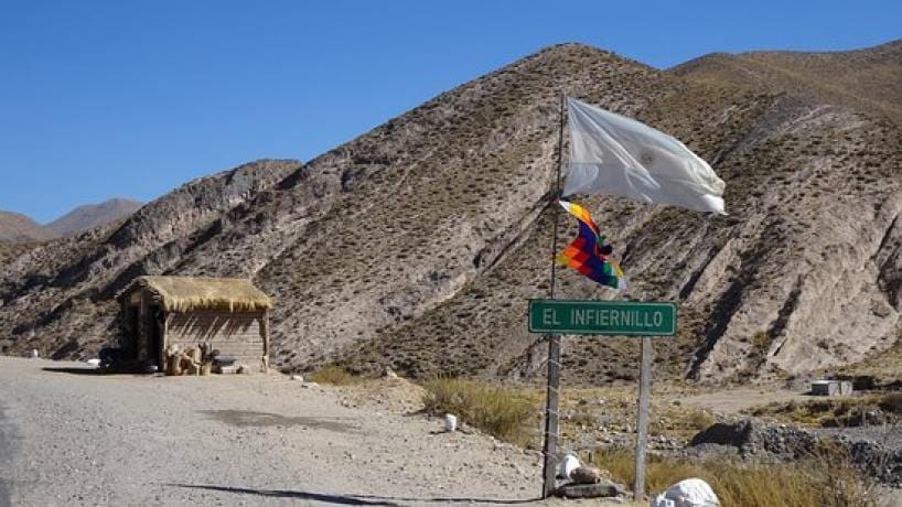 El cartel de ruta de El Infiernillo, con la bandera argentina y la wiphala flameando