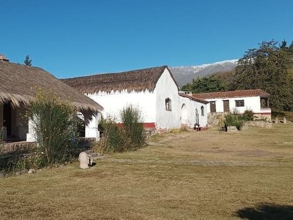 El casco de estancia del museo, con su techo de paja y la capilla, frente a los cerros nevados
